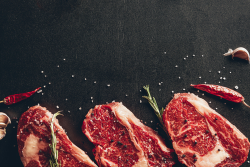elevated view of raw meat steaks and spices on surface in kitchen